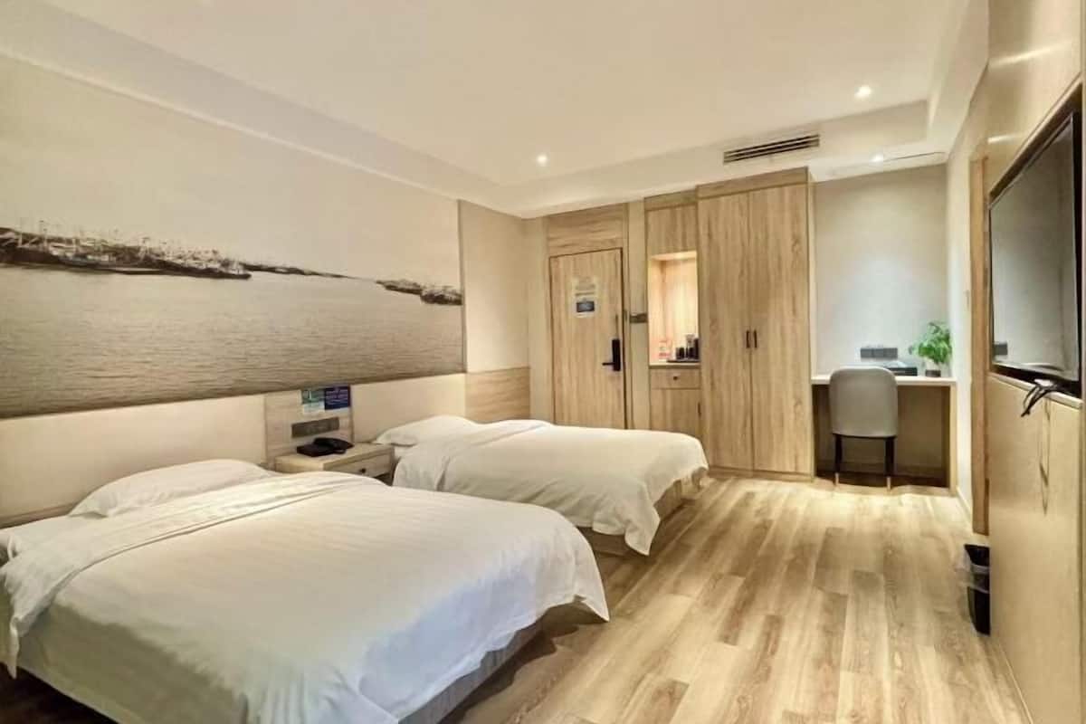 A hotel room with two beds, a desk, a chair, a wardrobe, and a large artwork on the wall.