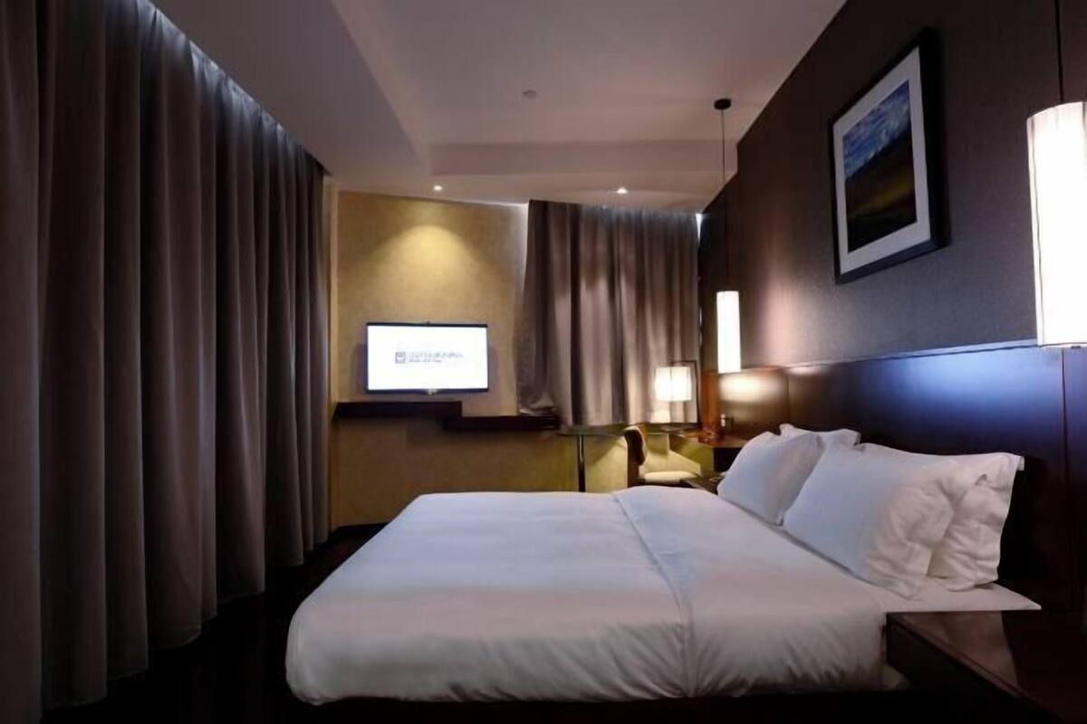 A hotel room with a large bed, a desk with a computer, a chair, and a TV screen.