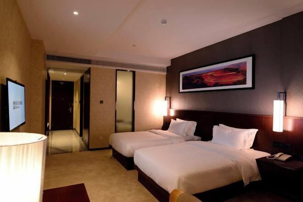 A hotel room with two beds, a TV, a painting on the wall, and a phone on the nightstand.
