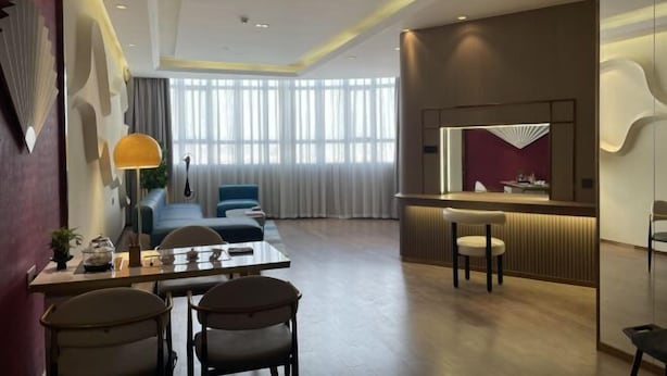 A modern hotel room with a dining area, a sofa, a desk with chairs, a large window with curtains, and a reception desk. - Babala Hotel (Guangzhou Dagang) (Guangzhou)
