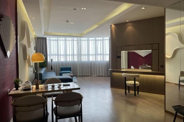 A modern hotel room with a dining area, a sofa, a desk with chairs, a large window with curtains, and a reception desk. - Babala Hotel (Guangzhou Dagang) (Guangzhou)