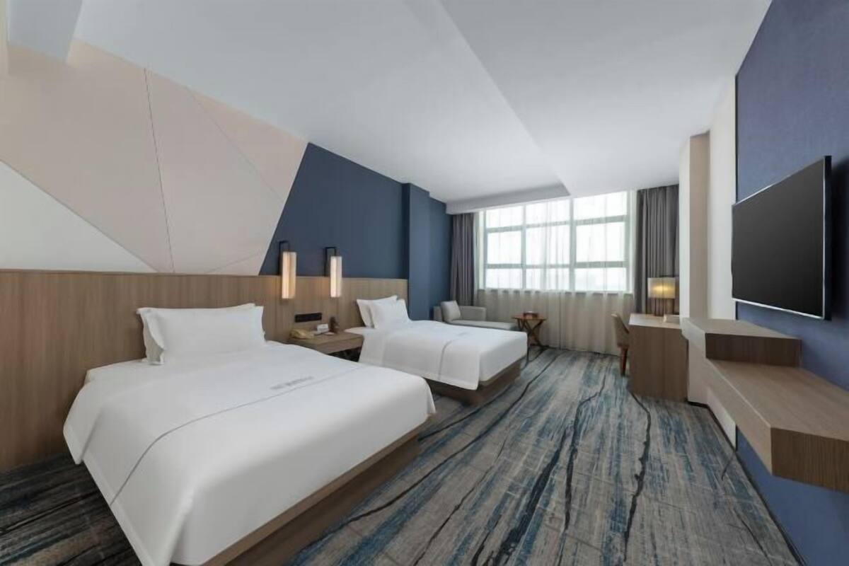 A hotel room with two beds, a TV, a desk, and a large window.