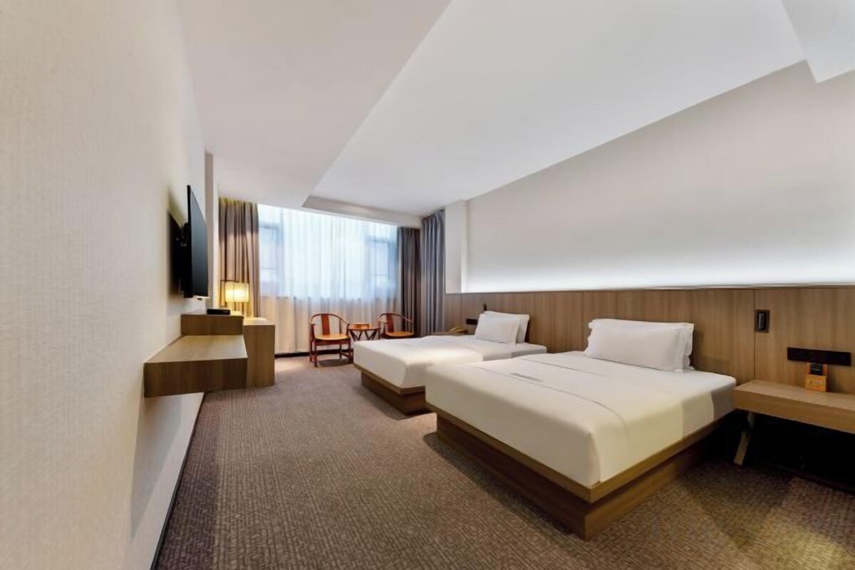 A hotel room with two beds, a desk, a chair, and a TV.