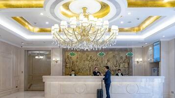 A hotel reception area with a large chandelier, a reception desk, and a wall mural.