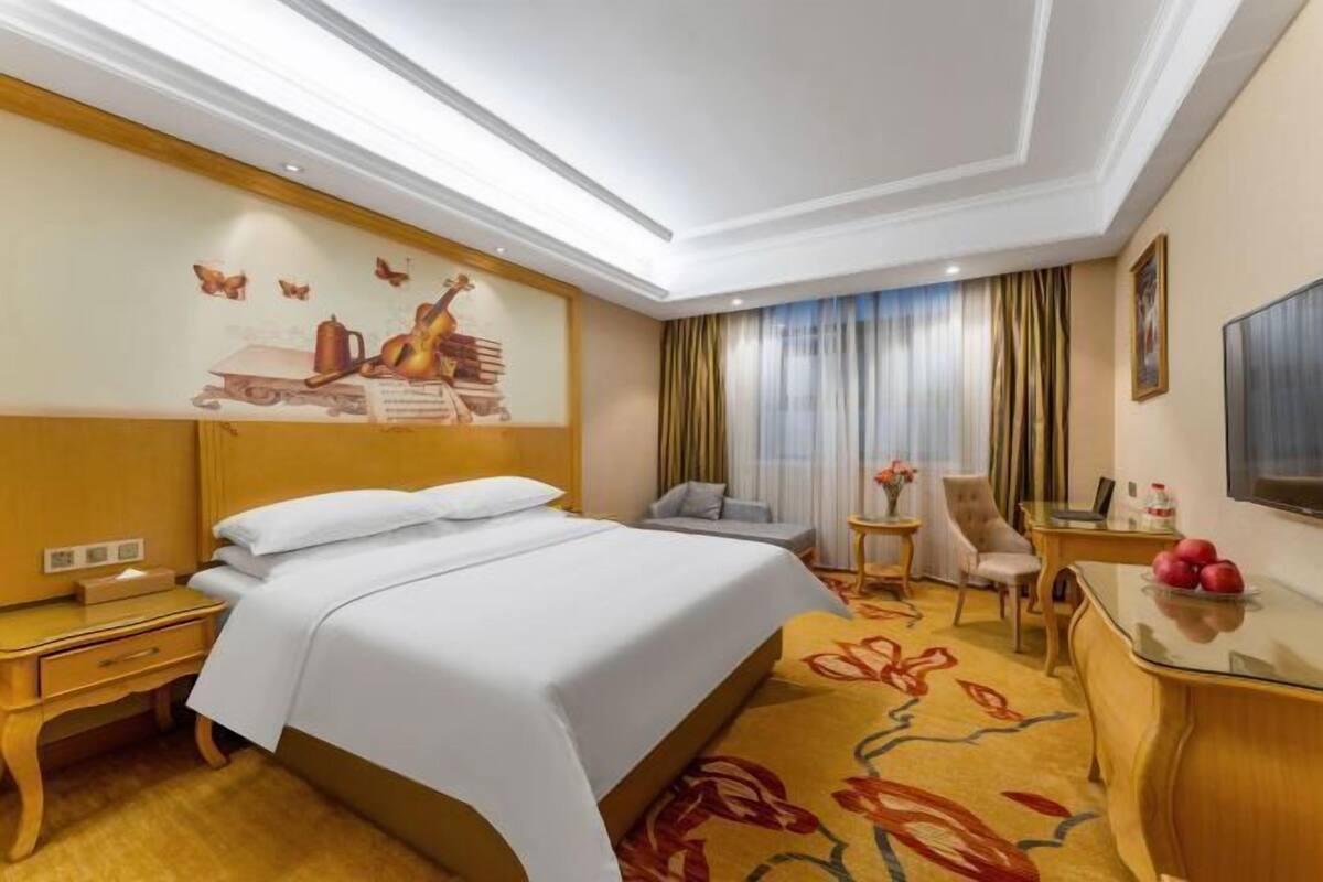 A hotel room with a bed, a desk, a chair, a small table, and a TV.