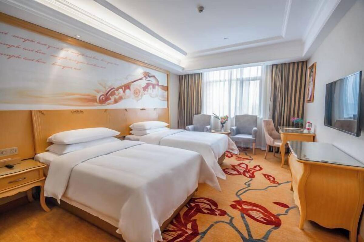 A hotel room with two beds, a desk, a chair, and a television.