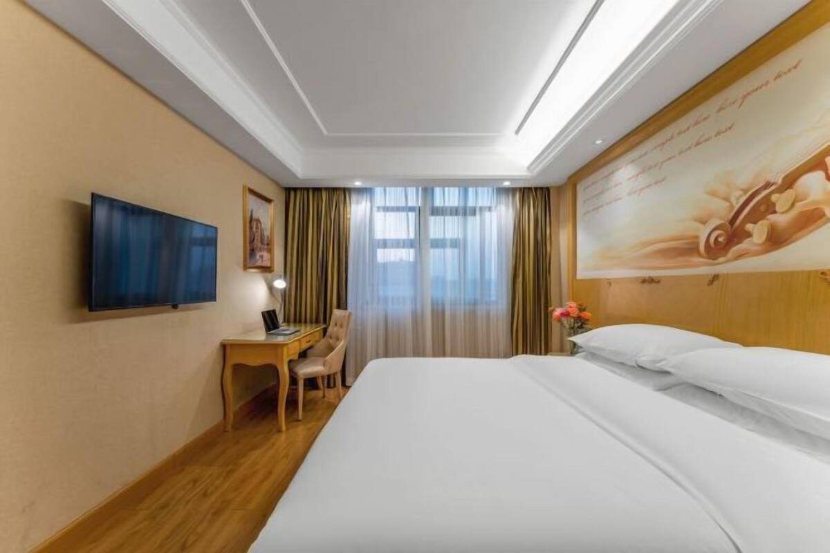 A hotel room with a bed, a desk, a chair, a television, and a window with curtains.