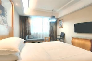 Una habitación de hotel con una cama grande, un sofá, una mesita, una silla y un televisor en la pared.