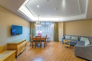 A modern living room with a flat-screen TV, a dining table with chairs, a sofa, and a small round table.
