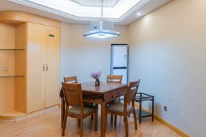 A dining area with a wooden table and chairs, a small vase with flowers, a ceiling light fixture, and a wardrobe.
