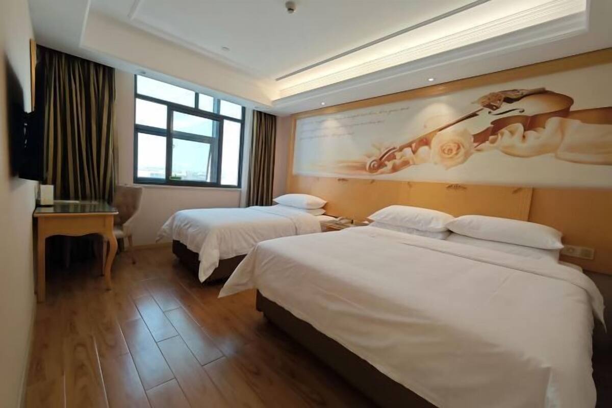 A hotel room with two beds, a desk, a chair, a TV, and a large window.