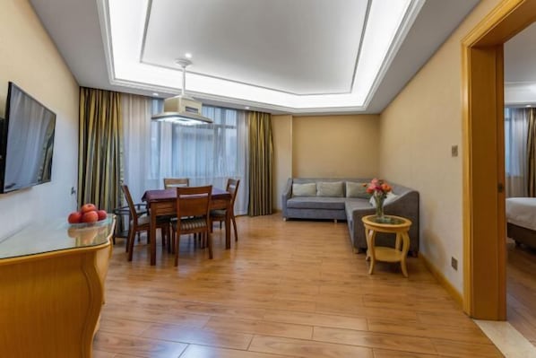 A compact hotel room with a dining area, a sofa, and a small side table with a vase.