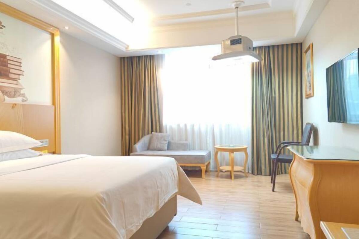 A hotel room with a bed, a sofa, a desk, and a TV.