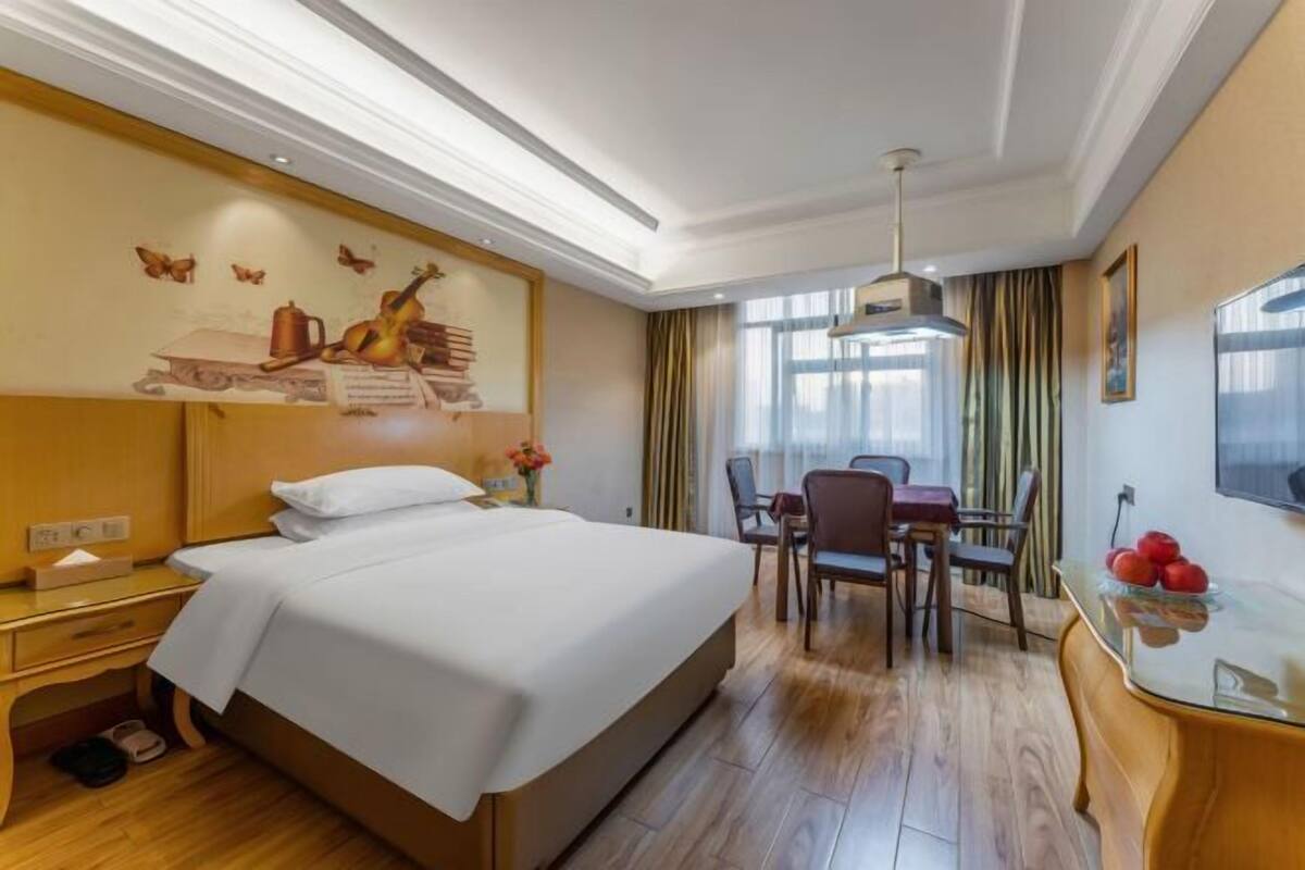 A hotel room with a bed, a desk, a chair, a dining table, and a window with curtains.