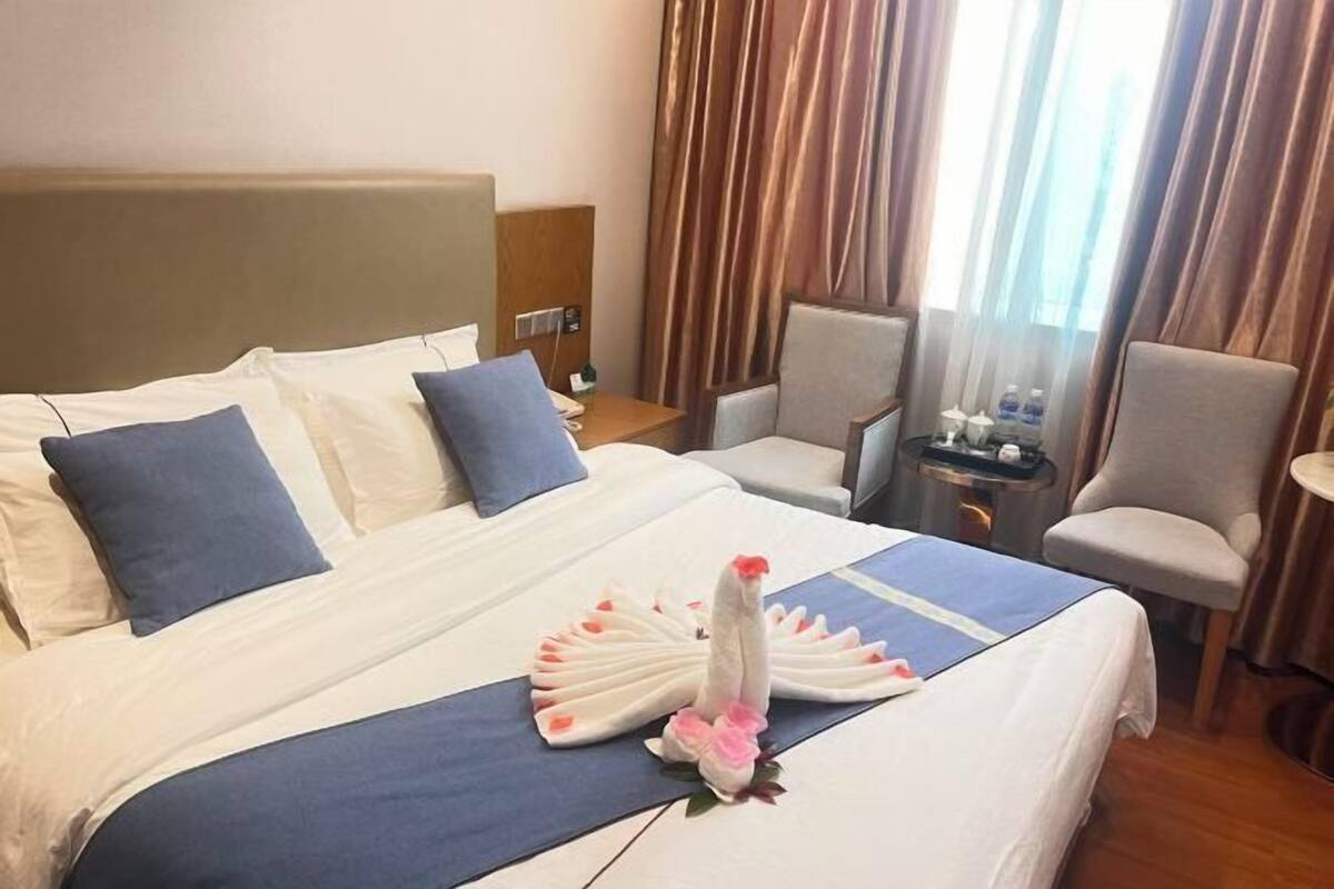 Habitación de hotel con cama, dos sillas, una mesita y una ventana con cortinas.