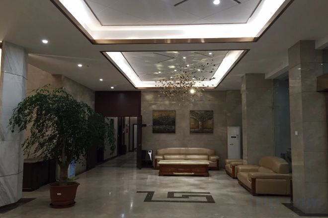 A modern lobby with a reception desk, seating area, and a large potted plant.