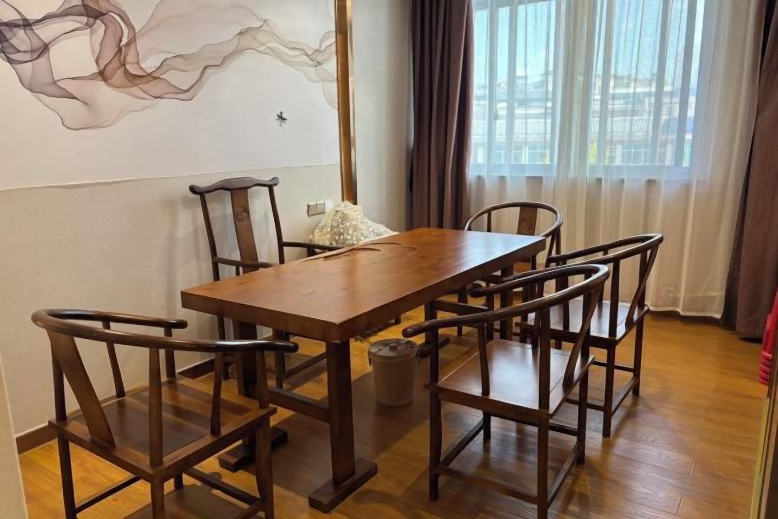 A dining area with a wooden table and chairs, a wall with abstract art, and a window with curtains.
