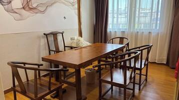 A dining area with a wooden table and chairs, a wall with abstract art, and a window with curtains.
