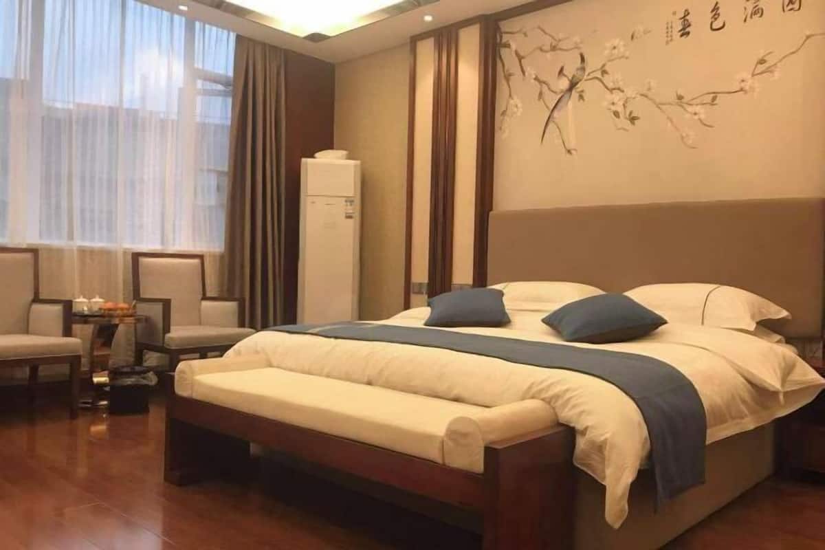 Habitación de hotel con cama, mesitas de noche, una silla, una pequeña mesa con lámpara y un adorno en la pared.