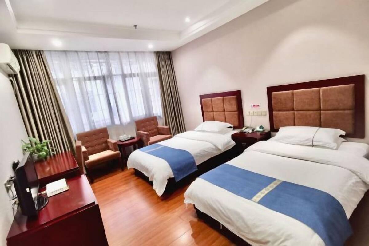 Una habitación de hotel con dos camas, un escritorio, una silla y una ventana con cortinas.