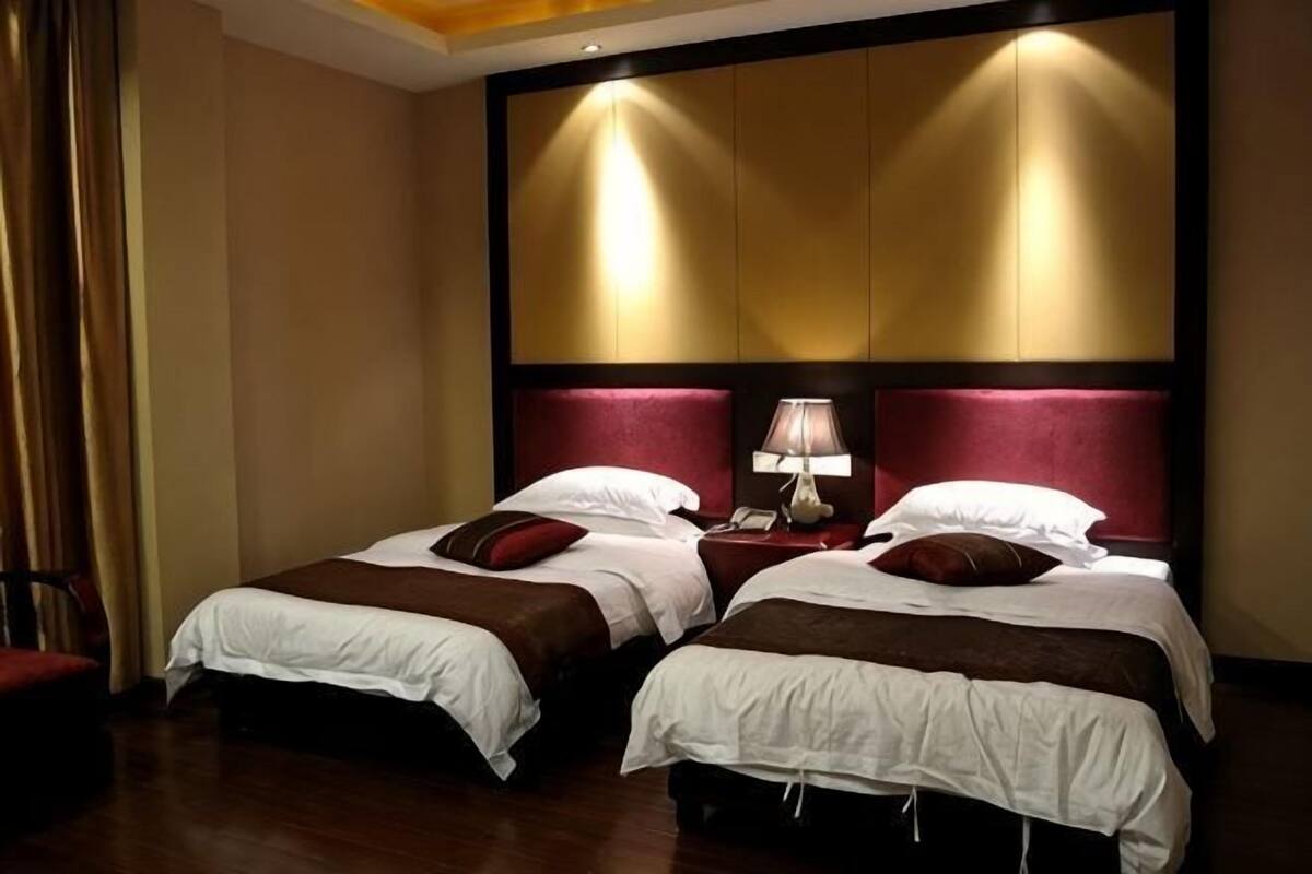 Una habitación de hotel con dos camas, una mesita de noche con lámpara y un panel grande en la pared.