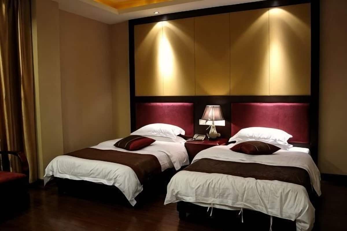 A hotel room with two beds, a nightstand with a lamp, and a large wall panel.