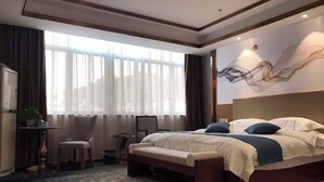 A hotel room with a large bed, a bench, a desk with a chair, a small table with a plant, and a large window with curtains. - Xunwu Hotel (Xunwu)
