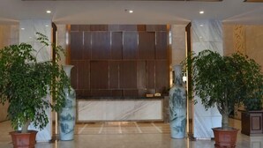 A lobby with marble reception desk, potted plants, and a modern light fixture. - Xunwu Hotel (Xunwu)