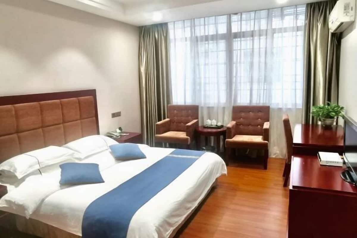 Habitación de hotel con una cama grande, dos sillones, una mesita, un escritorio y una planta en maceta.