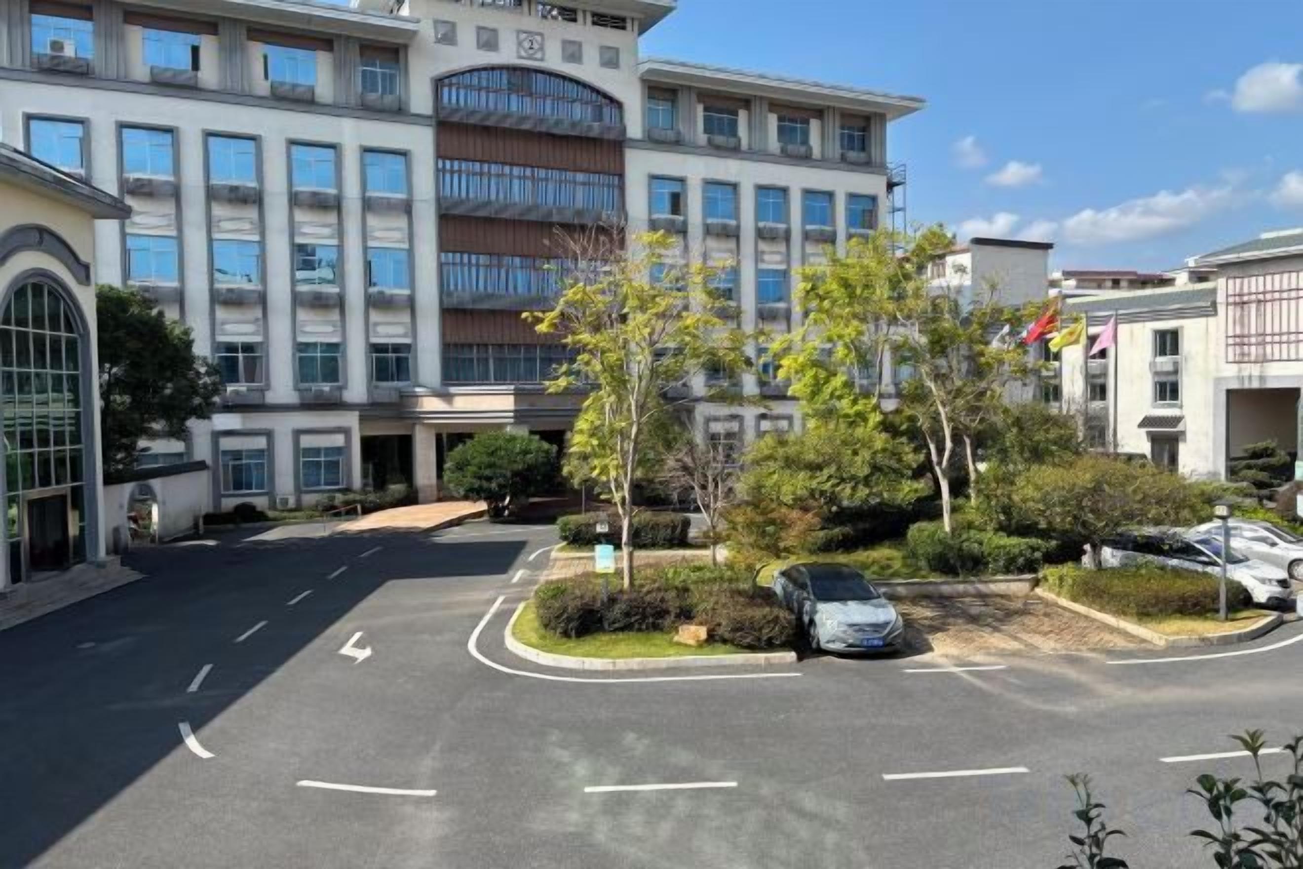 A multi-story building with a parking lot, a few trees, and a clear sky.