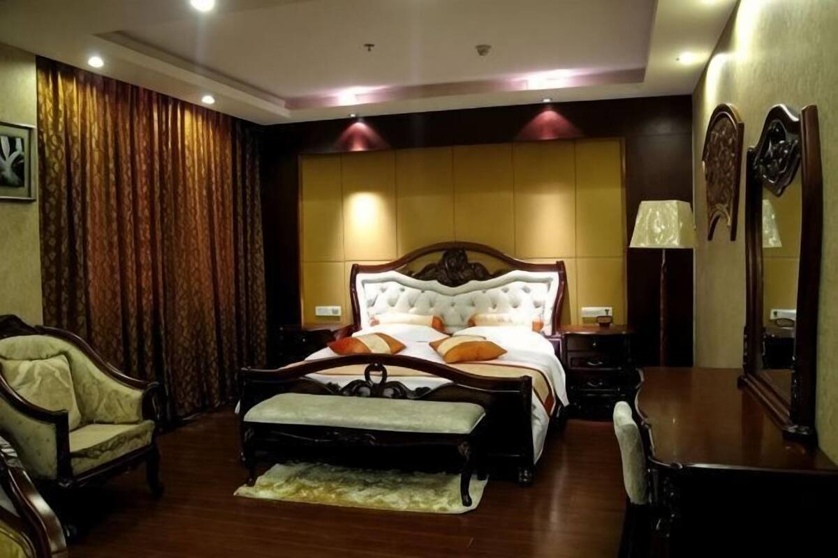 Un dormitorio con una cama grande, un banco de madera, una silla, una mesita de noche y un espejo.