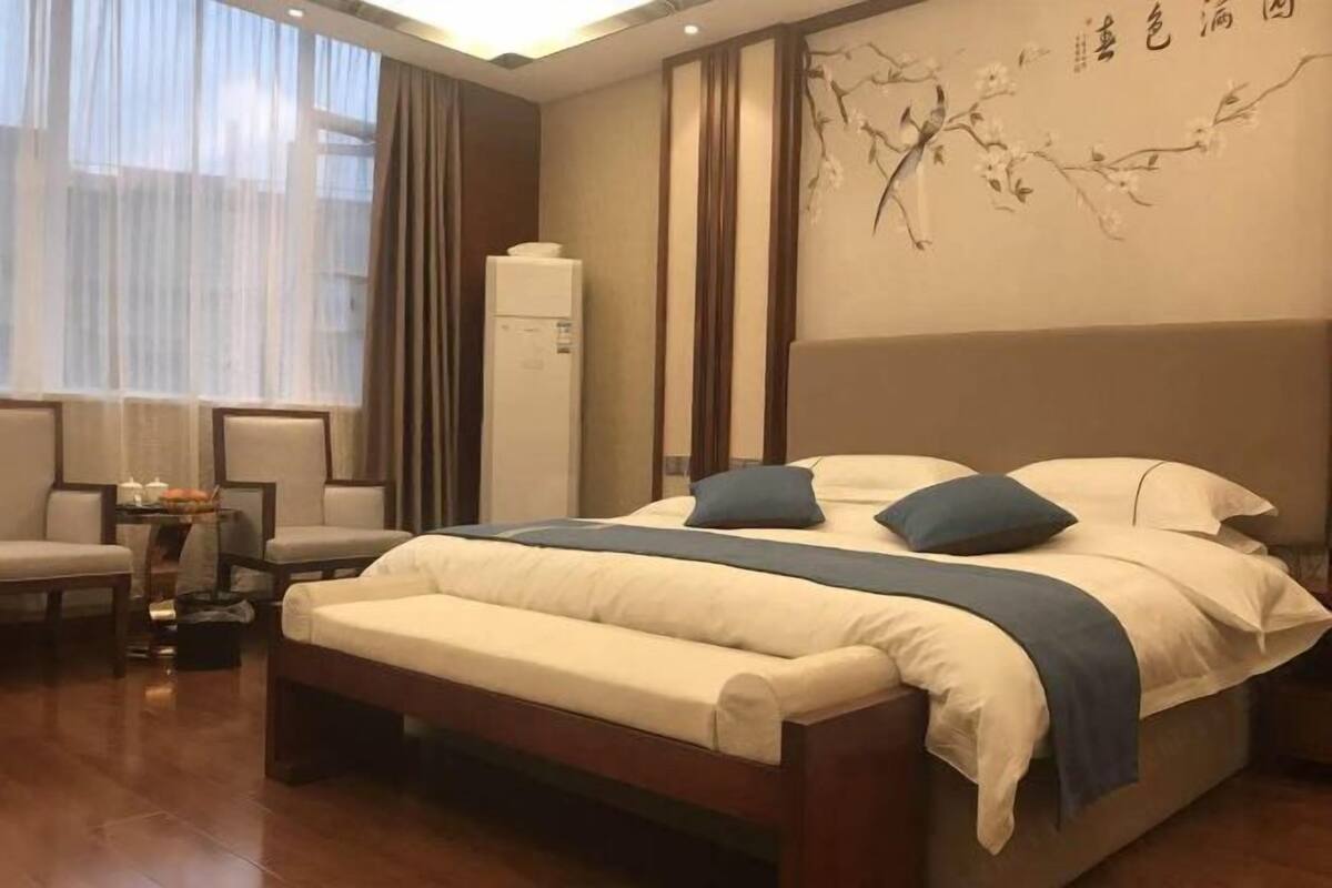 Un dormitorio con cama, mesitas de noche, una silla, una pequeña mesa con lámpara y una pared con diseño de ramas.