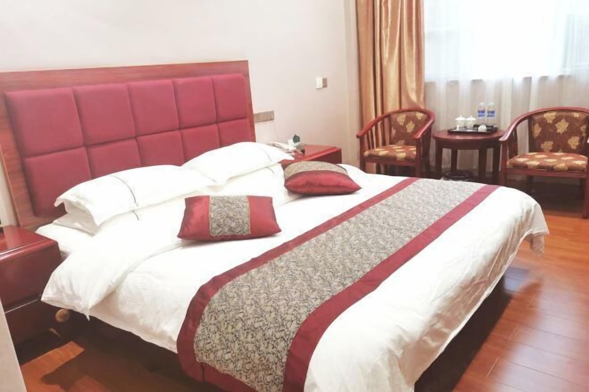 Ein Hotelzimmer mit einem großen Bett, zwei Nachttischen, einem kleinen Tisch mit Stühlen und einem Fenster mit Vorhängen.