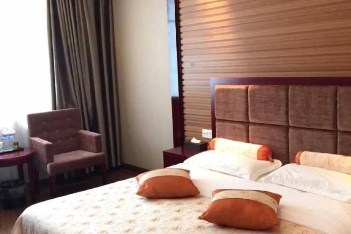 Habitación de hotel con una cama grande, una silla, una mesita de noche y un cabecero de madera.