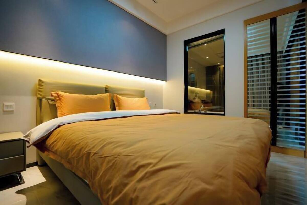 Un dormitorio moderno con una cama grande, mesitas de noche y un gran ventanal corredizo.