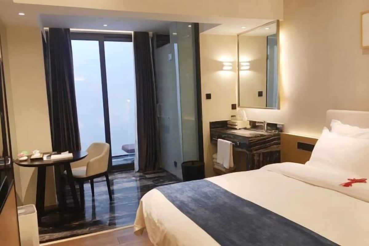 Habitación de hotel con cama, escritorio, silla, baño y vistas al exterior.