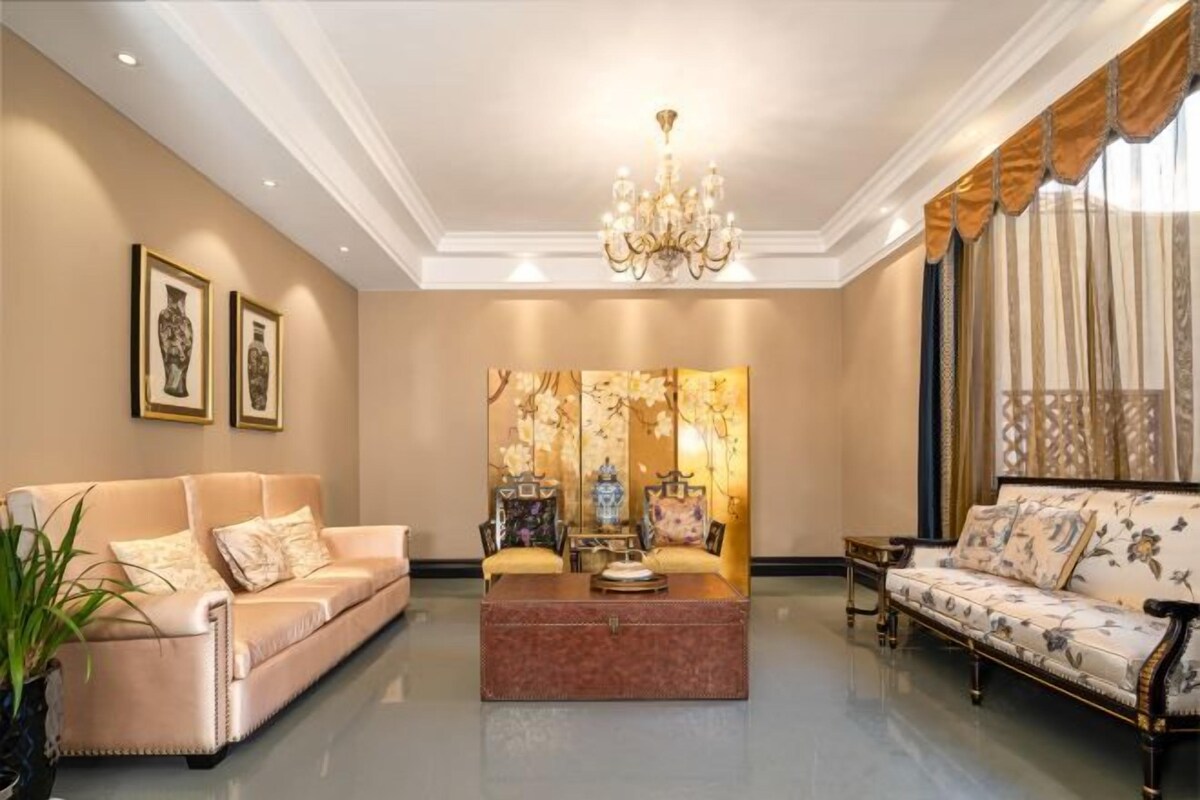 A spacious living room with a beige sofa, a matching armchair, a coffee table, and a decorative screen.