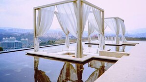 Piscina infinita no terraço, com toldos brancos e vista para o horizonte urbano.