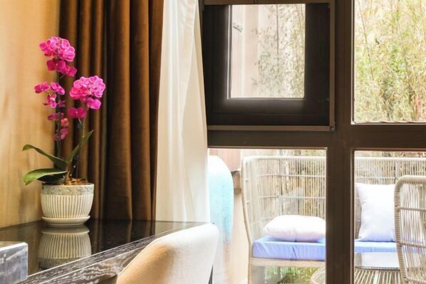 A room with a view of greenery through a window, wicker furniture, and a potted orchid.