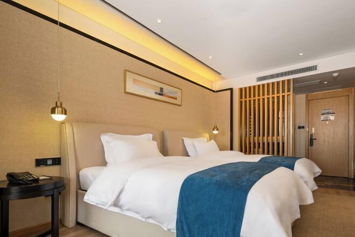 A hotel room with two beds, a bedside table with a phone, a wall-mounted light, and a wooden partition.