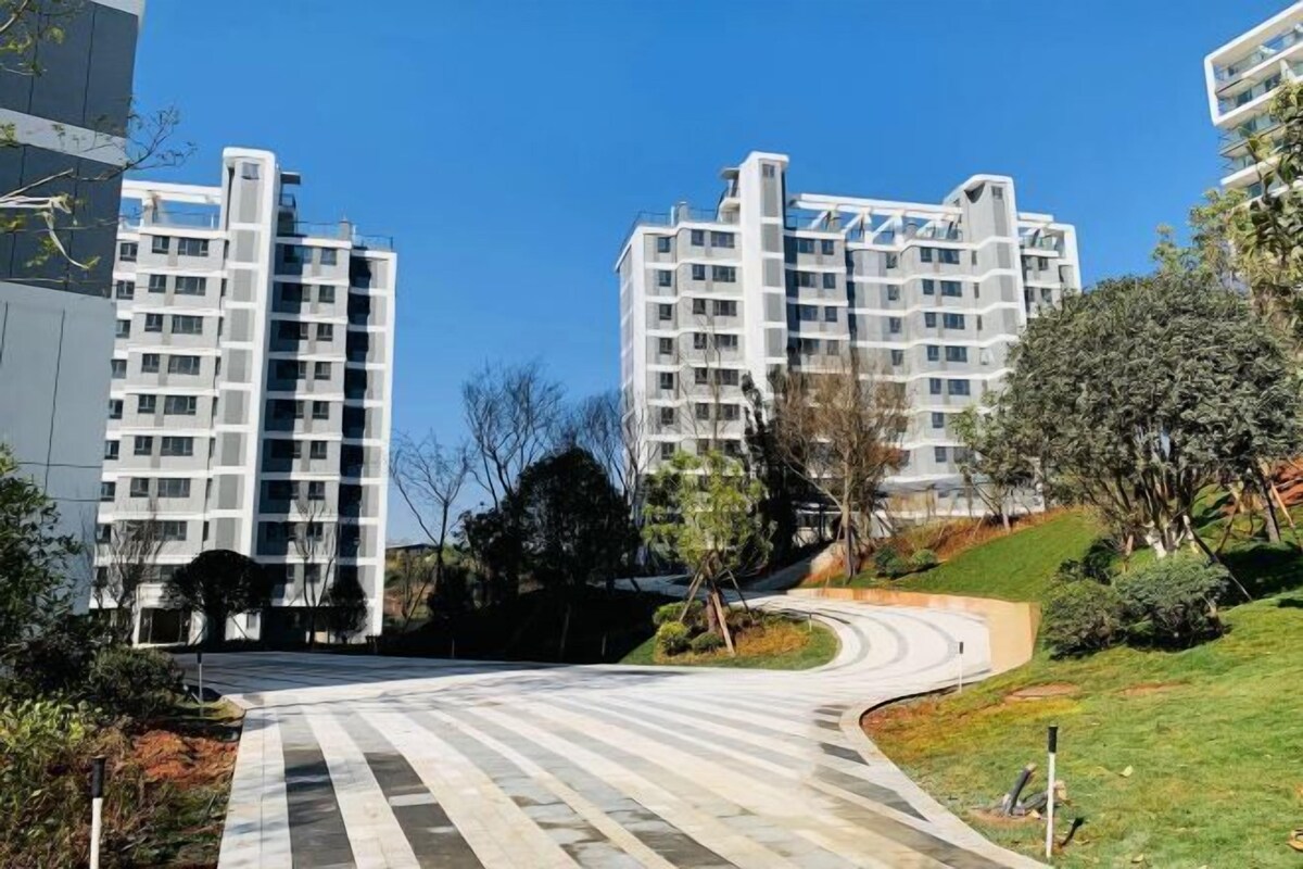 A modern residential building with a curved driveway and landscaped surroundings.
