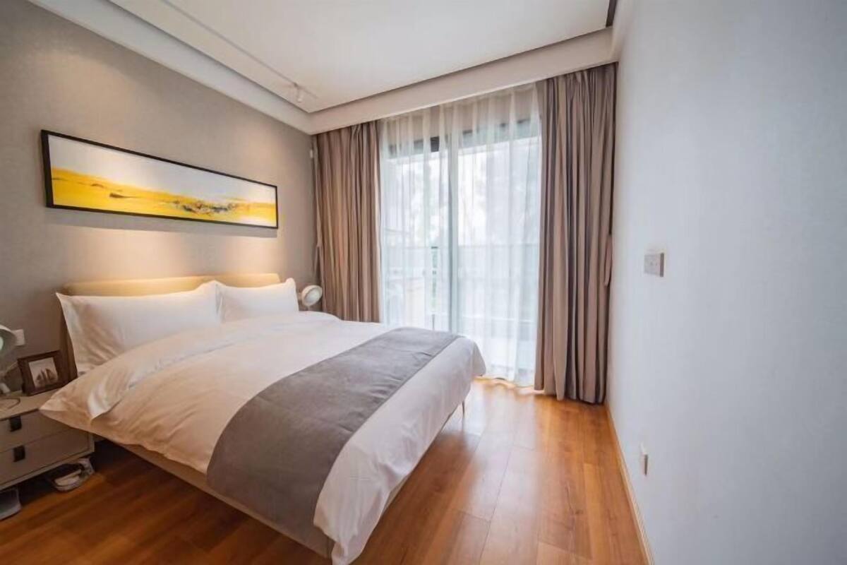 Un dormitorio moderno con una cama grande, una mesita de noche, una lámpara y una ventana con cortinas.