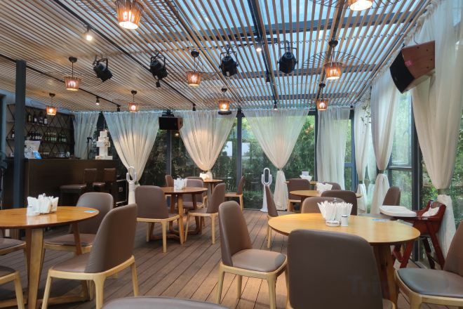 An indoor dining area with tables and chairs, a bar area, and a ceiling with exposed beams and lighting fixtures.
