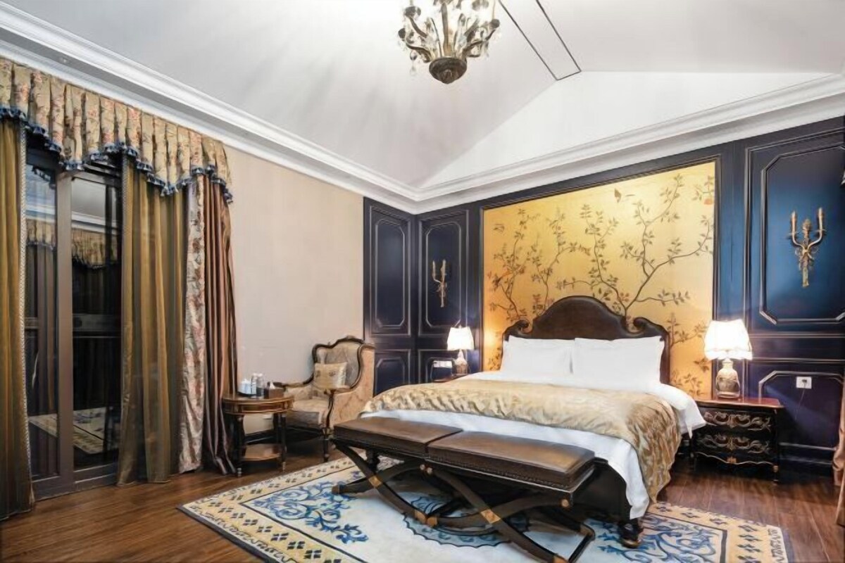 A classic bedroom with a large bed, a bench, a nightstand, and a chandelier.