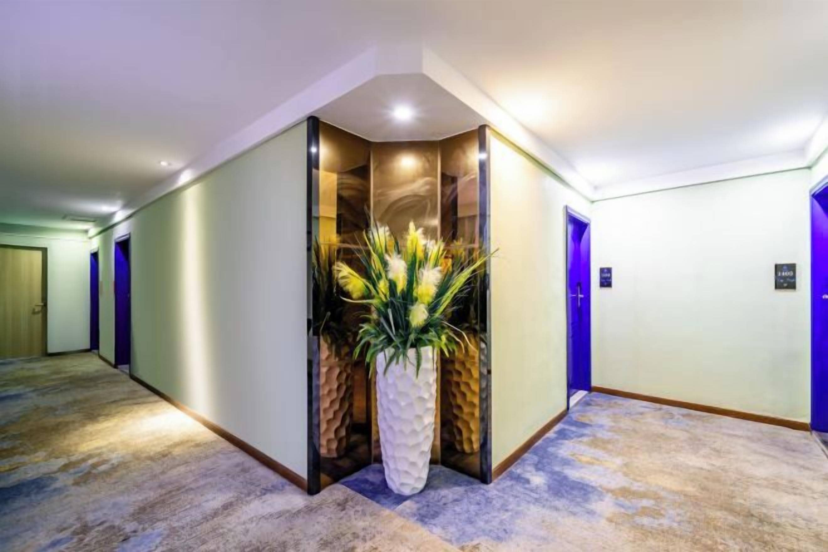 A hotel hallway with a corner reception area, carpeted flooring, and doors leading to rooms.