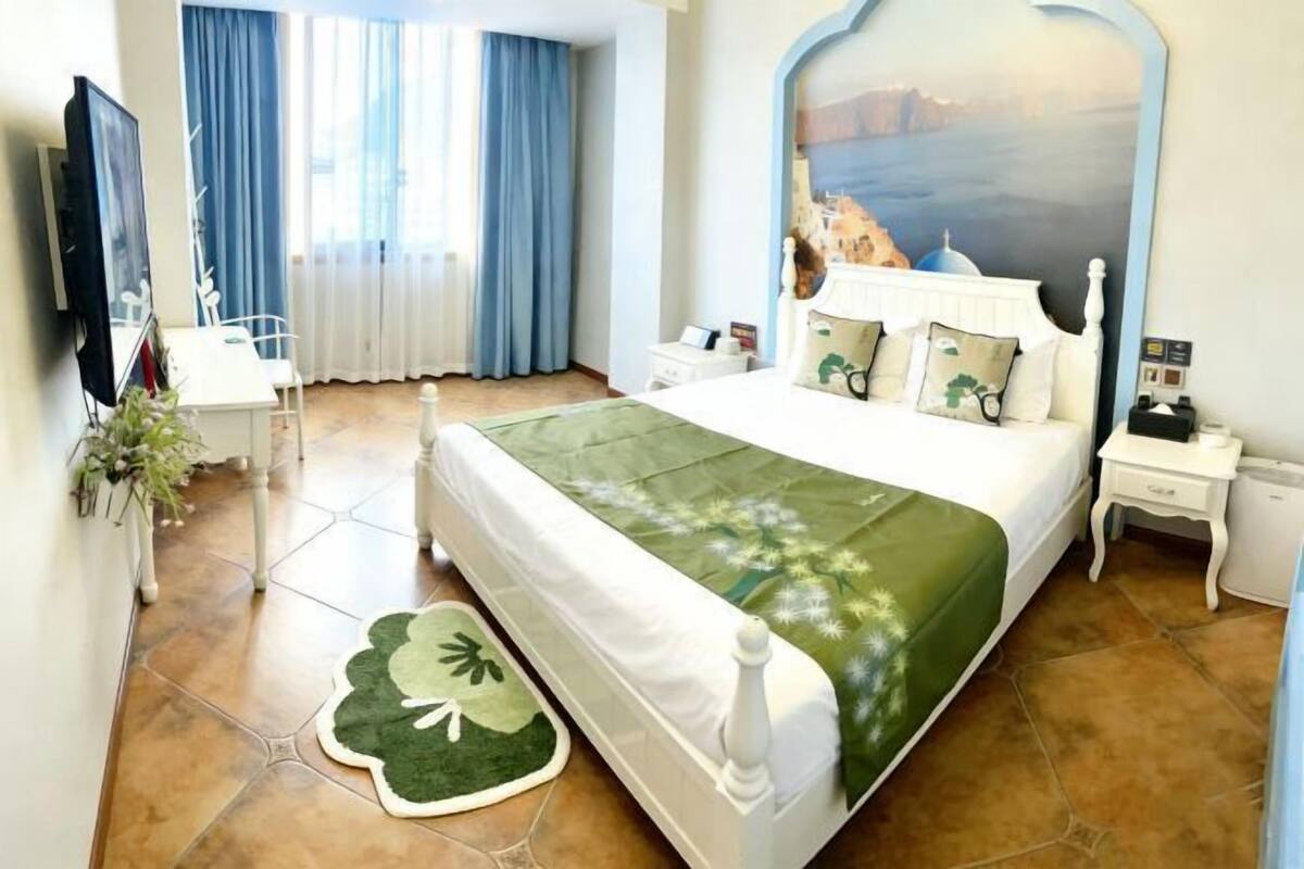 A hotel room with a bed, a nightstand, a TV, a window with curtains, and a wall painting.