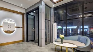 Un lobby moderno con mostrador de recepción, zona de estar con sofá y mesa, y grandes ventanales que ofrecen vistas al exterior.