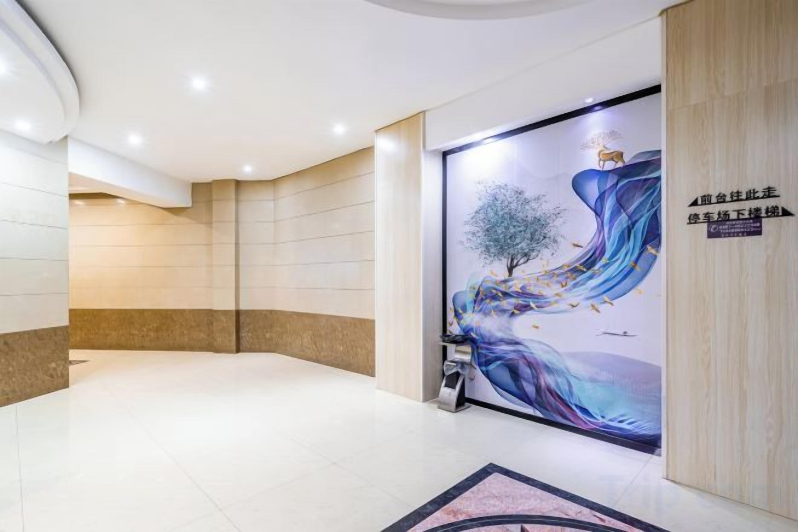 En hotellobby med et stort muralmaleri, en receptionsdisk og et skilt, der viser hotellets navn.