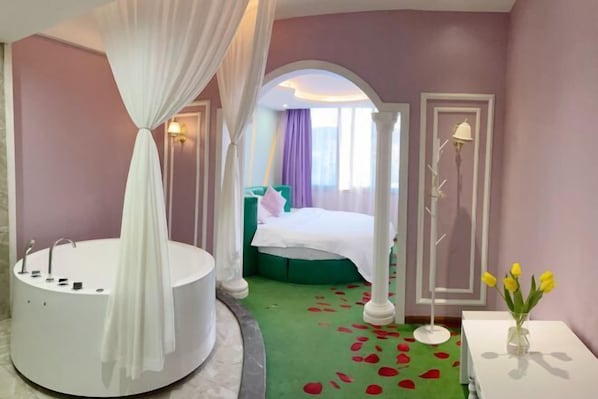 A bedroom with a large bathtub, a bed with green bedding, and a vase with yellow flowers on a white table. - Biyun Lanting Hotel (Zunyi Huizhi) (Zunyi)