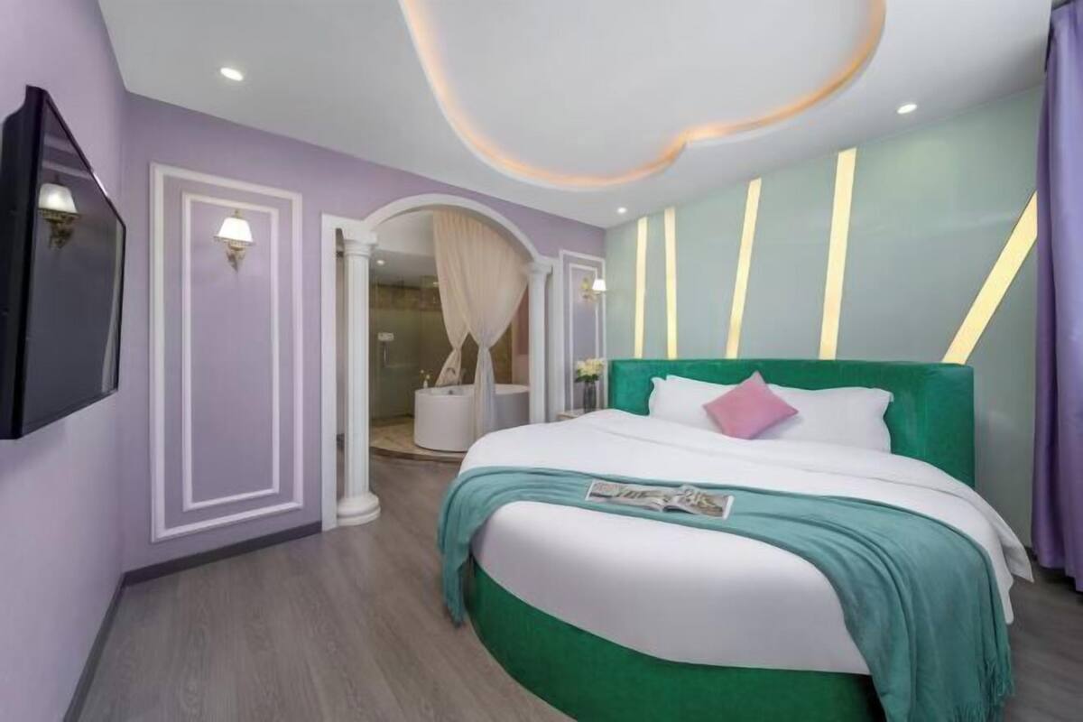 A modern bedroom with a green upholstered headboard, a white bedspread, and a teal throw blanket.